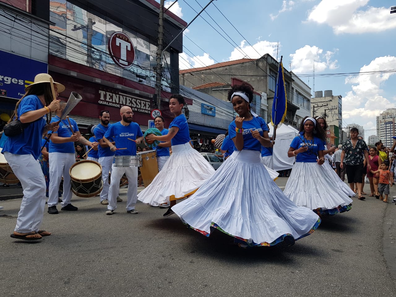 Grupo Maracatu na 12 de outubro dançarinos vestidos de branco e azul, mulheres com longos vestidos e homens com caça, camiseta e chapéu